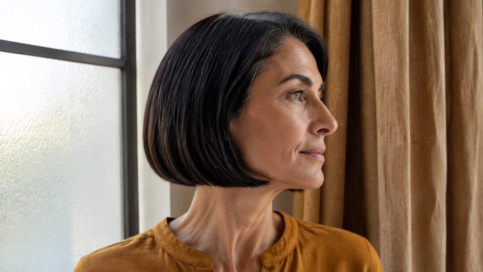 Mature adult in near profile with a straight dark chin bob, continuous jaw-level perimeter, and subtle silver strands