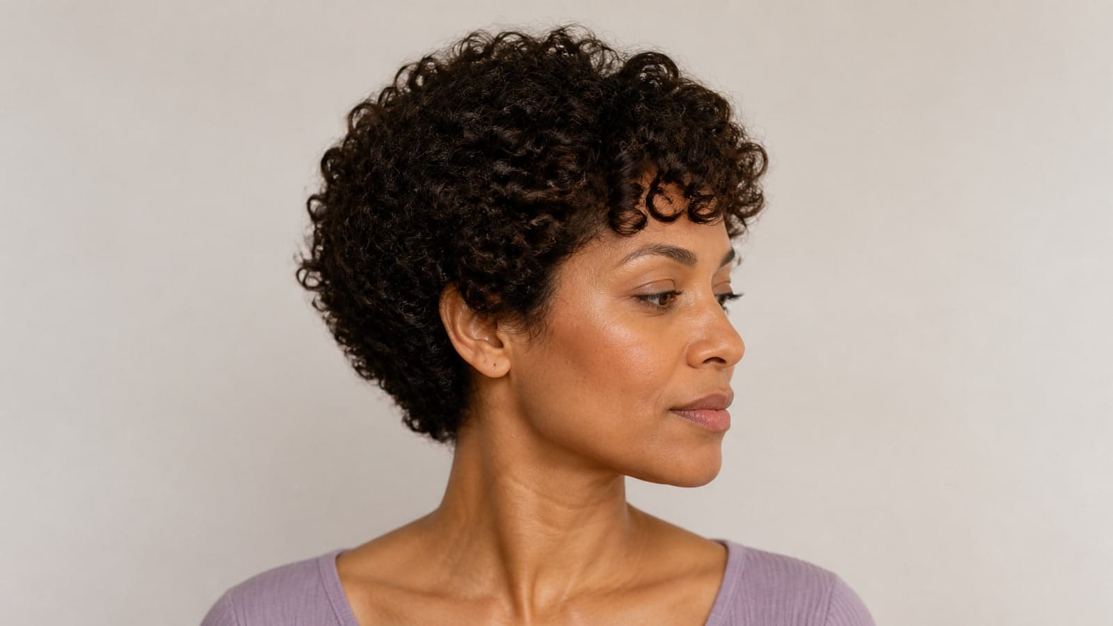 Curly crop with a rounded ear-level dry outline, graduated crown, curl fringe, and softly shaped neckline on defined curls